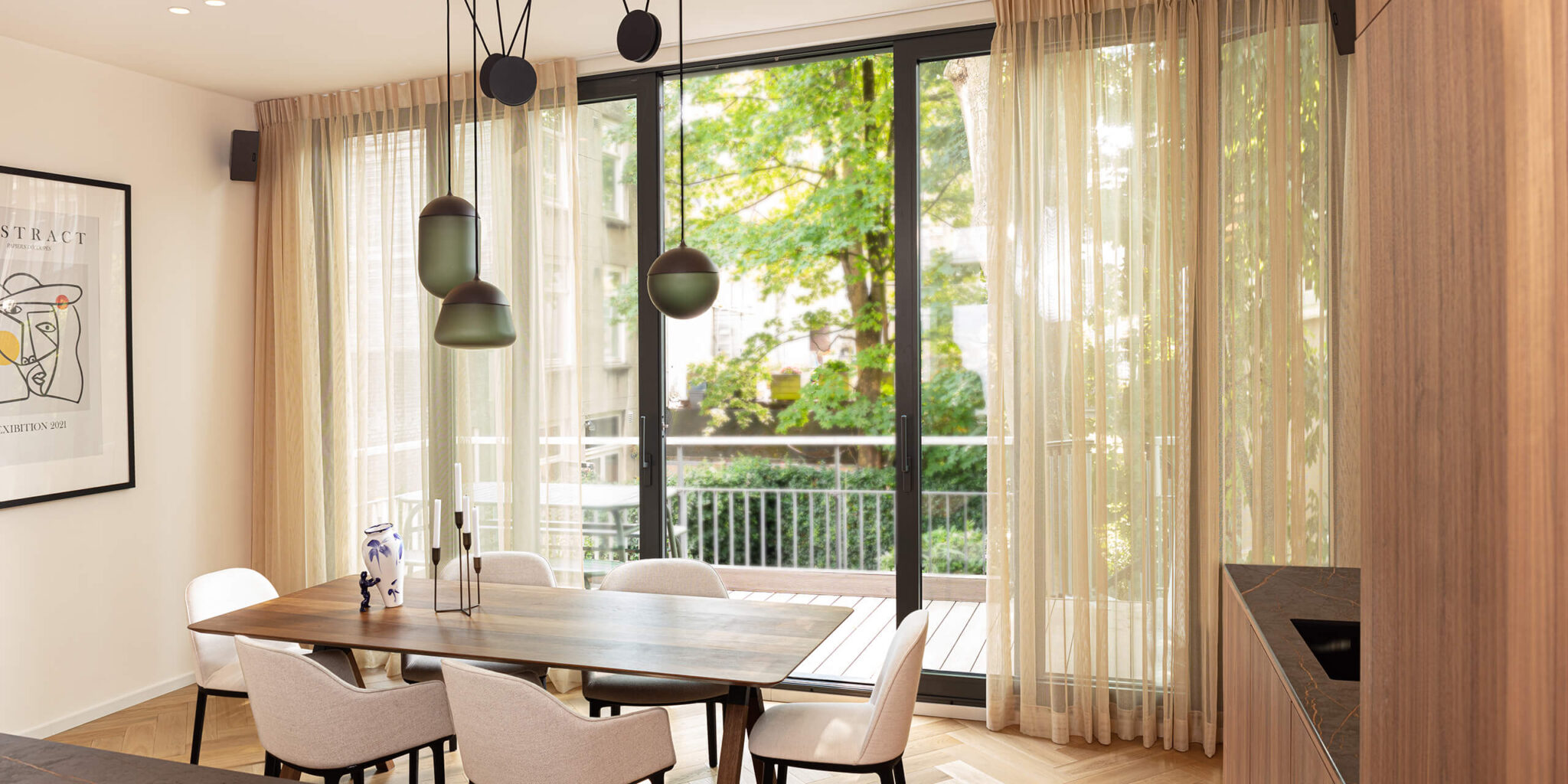 Elegant dining room with a wooden table, six white chairs, and Brokis Planets 3 Set. Glass doors frame lush balcony views.