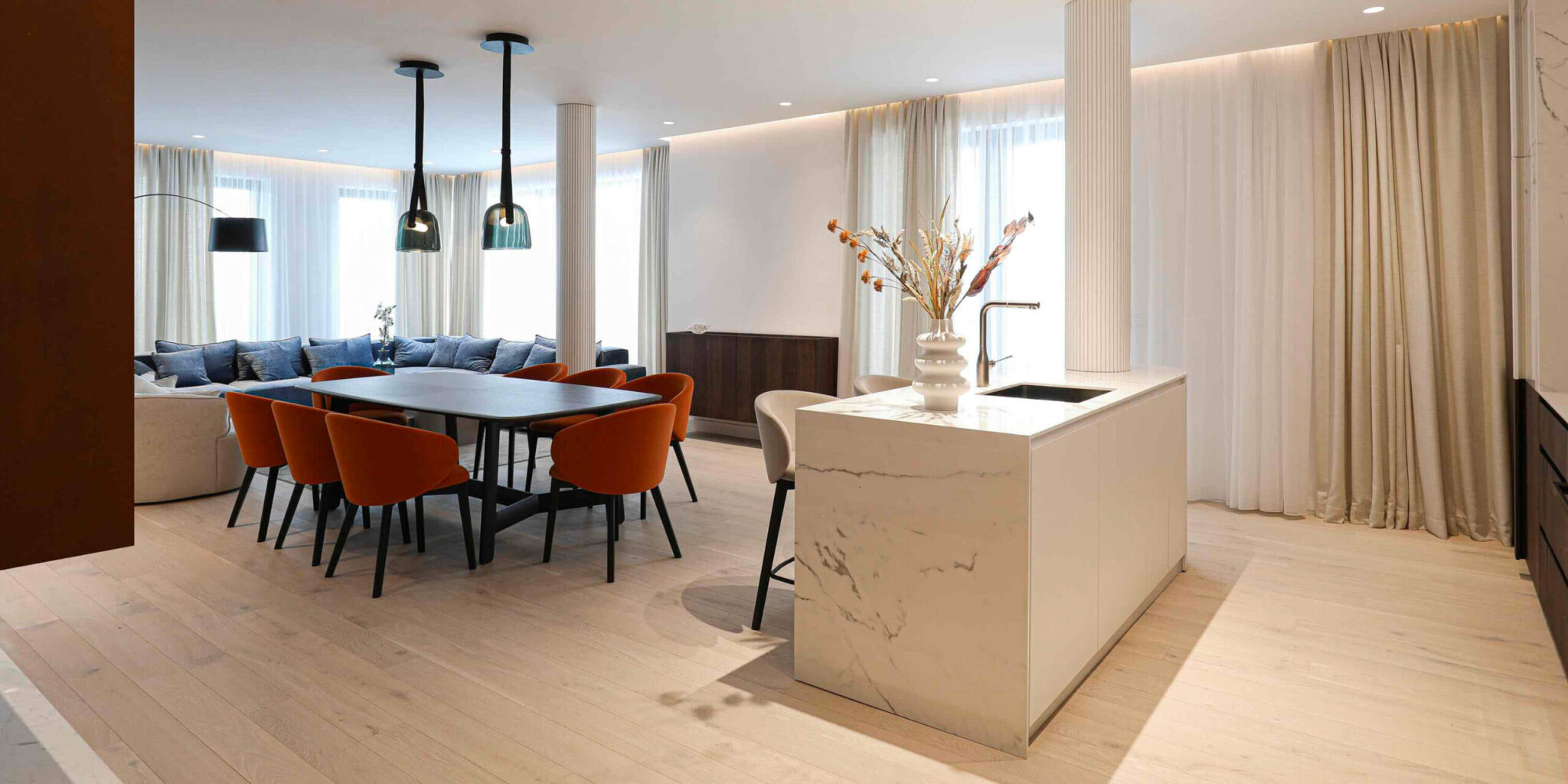 Sophisticated open-plan living and dining area with light wood floors, marble island, Mona Medium pendants, and luxe accents.