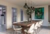 Modern dining room with a long wooden table, white chairs, Brokis Awa pendants, and bold portrait art.