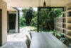 Modern dining area with long table, woven chairs, open bookshelves, stone floors, and Brokis Shadows Set Free.