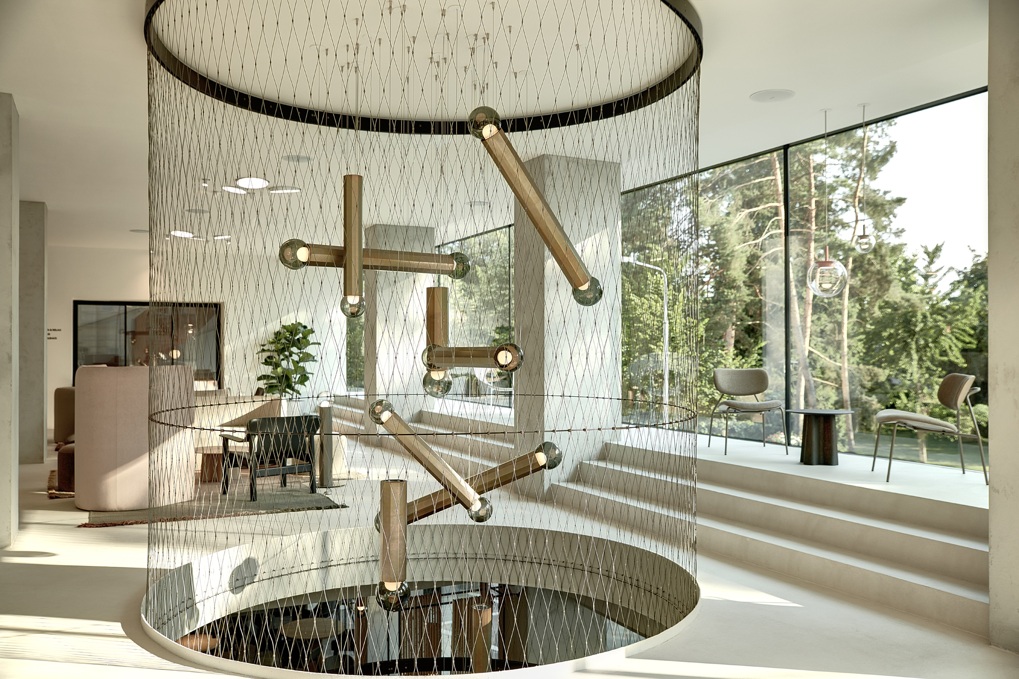 A sunlit modern interior with a circular stair enclosed by netted balustrade and Brokis Prisma pendants.