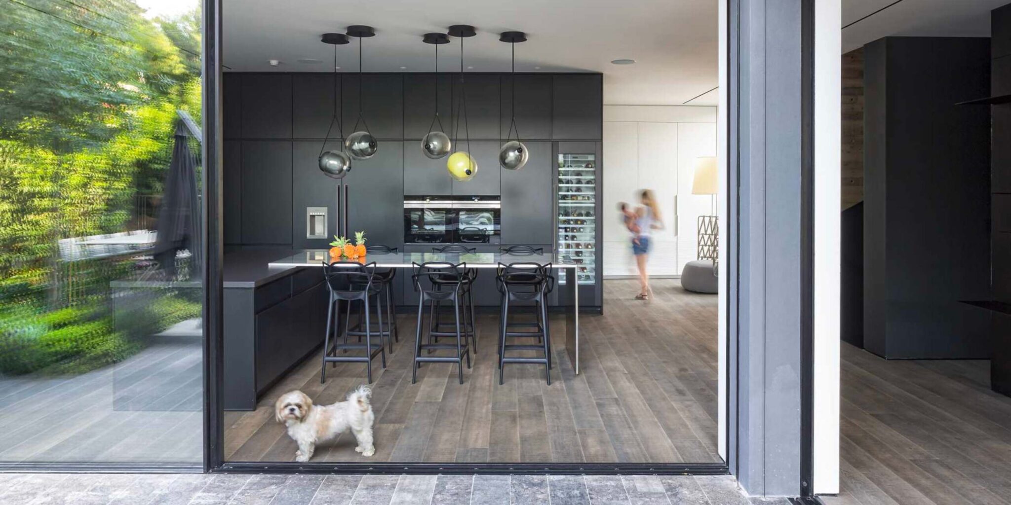 Luxury kitchen with black cabinetry, Capsula Single Pendants, breakfast bar, and garden views through glass doors.