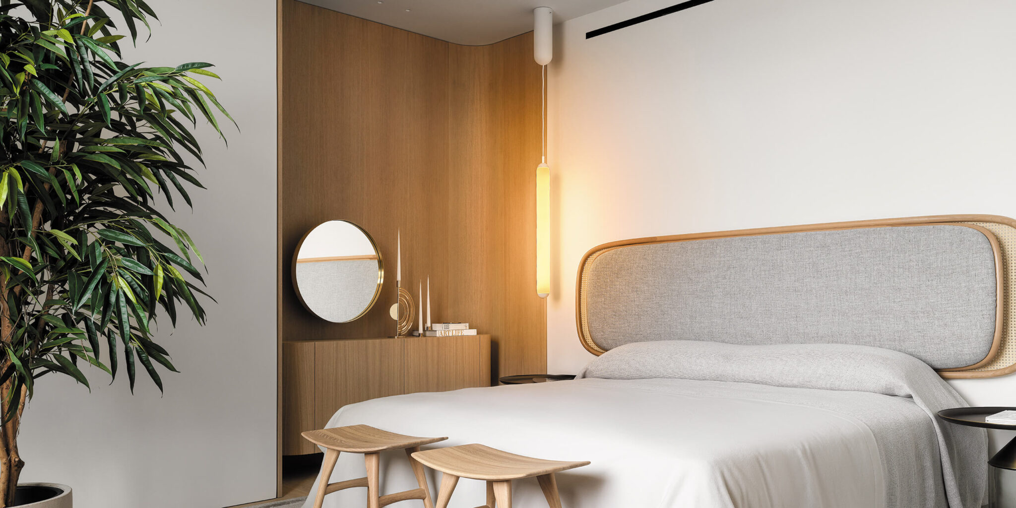Minimalist bedroom with a light grey upholstered headboard, sculptural Brokis Puro Solo, wooden stools, and luxe accents.