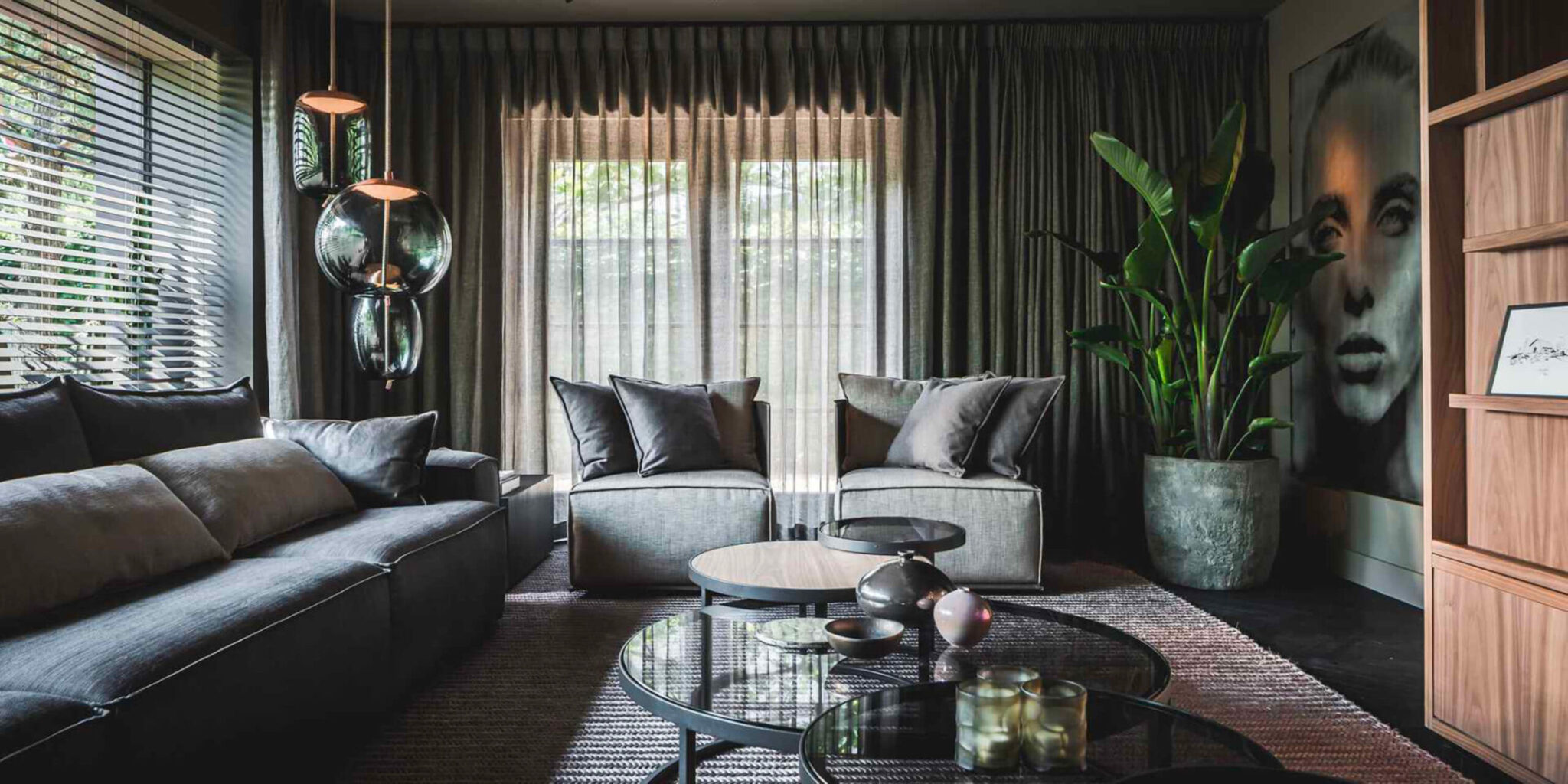 Elegant living room with sheer-draped windows, dark grey sofas, round glass tables, green plant, and Brokis Knot pendants.