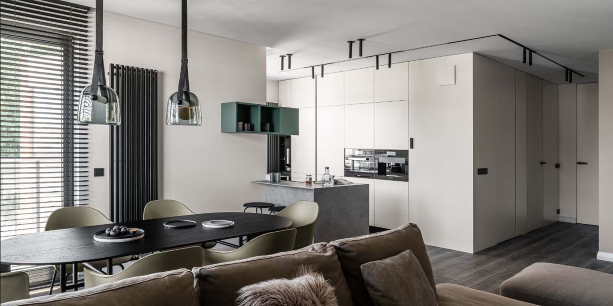 A open-plan kitchen boasts minimalist cupboards, a sleek island, Brokis Mona Medium lights, and floor-to-ceiling windows.