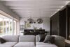 Open-plan living space with vast forest views, plush grey sofa, Brokis Big One Large pendants, and a minimalist kitchen.