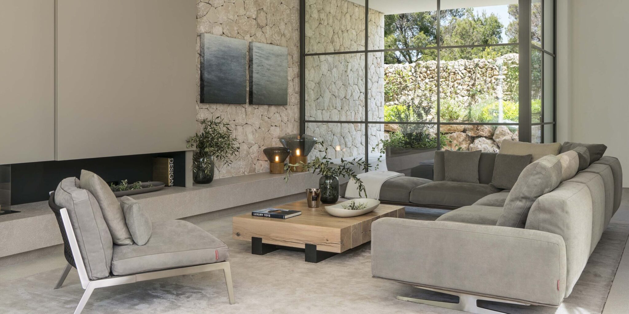 Elegant living room with stone feature wall, expansive windows, grey corner sofa, Muffins lighting, and sleek fireplace.