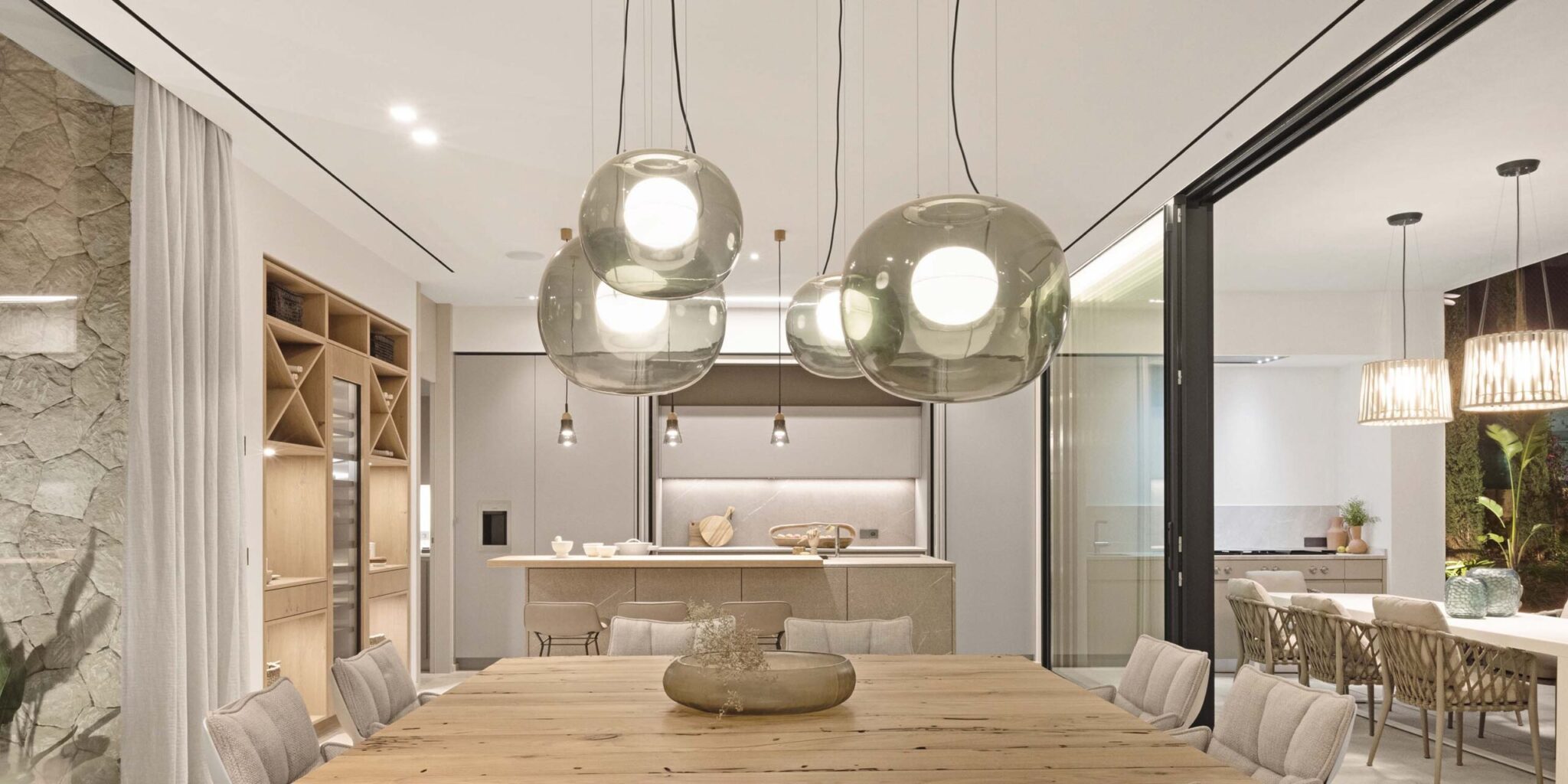 A sophisticated dining room with a large wooden table, cushioned chairs, and Brokis Big One Large pendants.