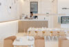 A modern, minimalist café with white walls, light wood furniture, playful chairs, elegant pendant lights, and laid tables.