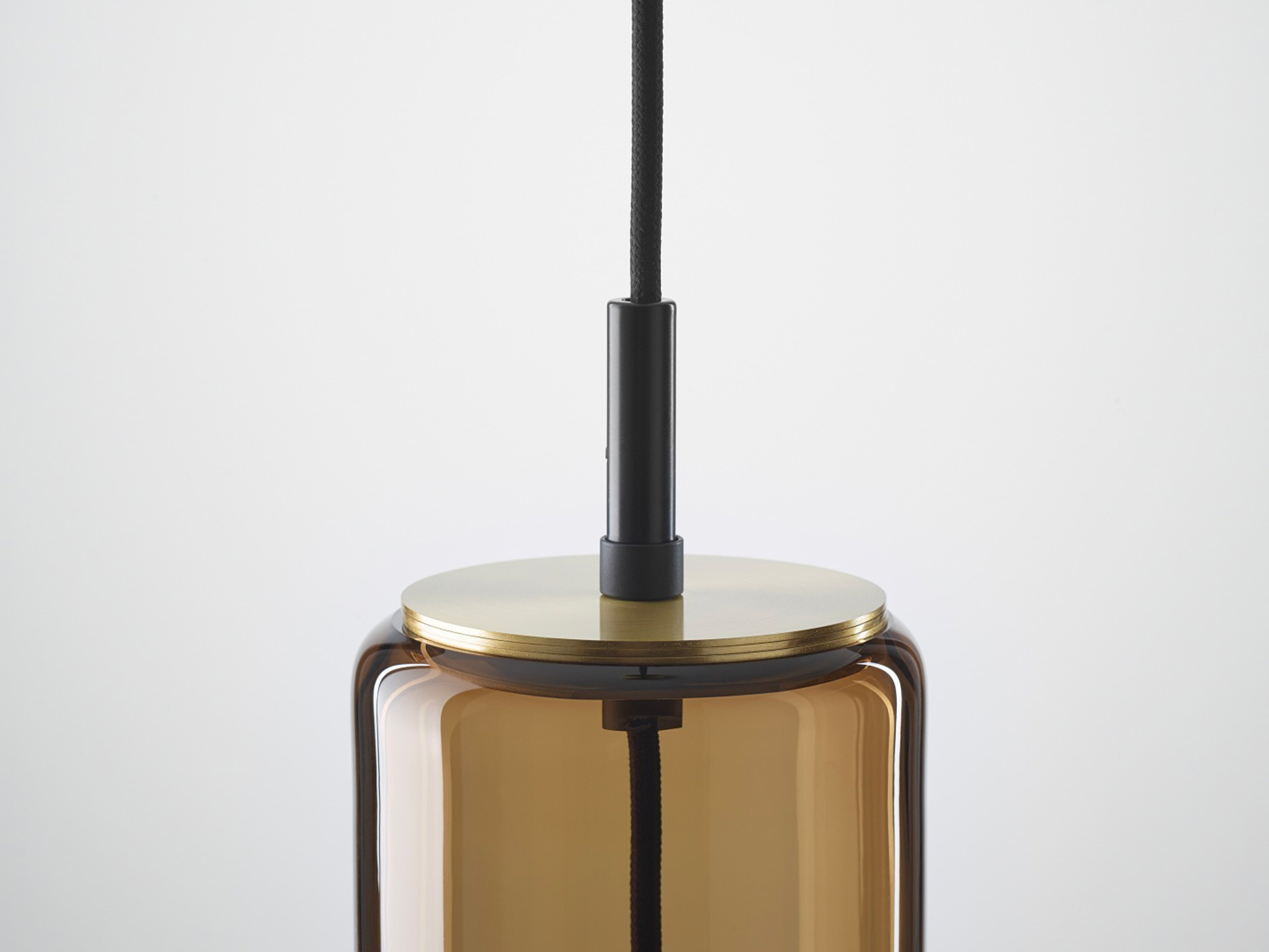 Close-up of a Brokis Whistle Medium, hand-blown brown glass cylinder, metallic brass top, and black cord on a white backdrop.