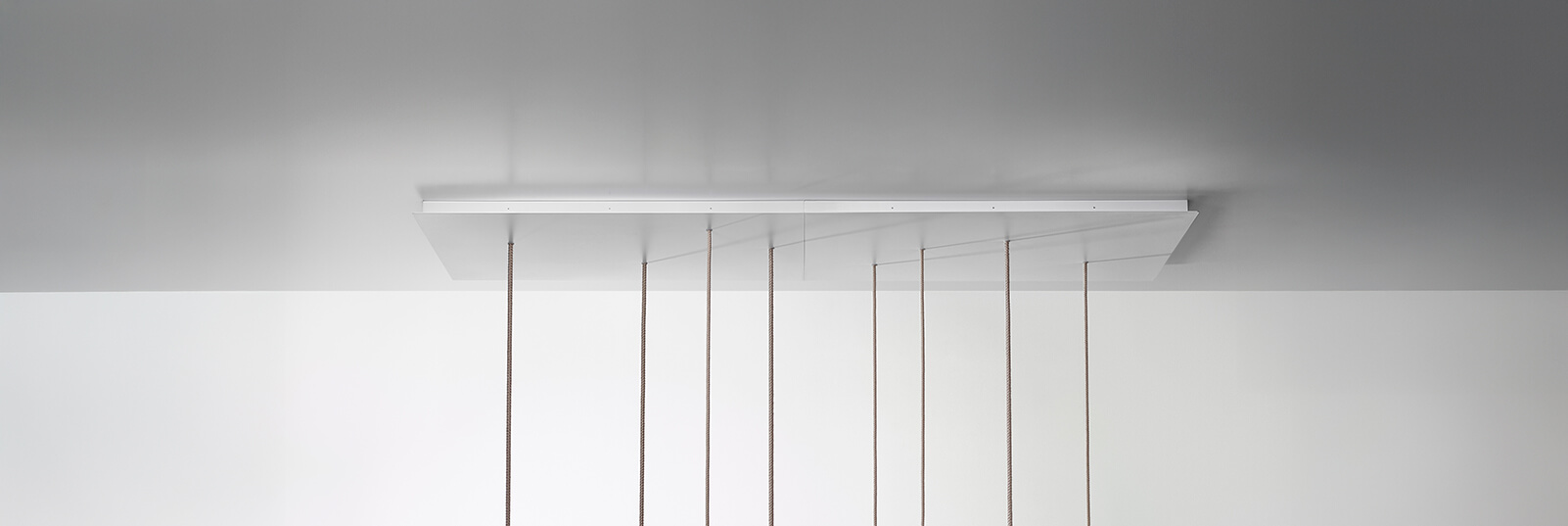 A sculptural ceiling fitting with a flat white panel and six lush cords, set against a sleek grey-and-white modern backdrop.