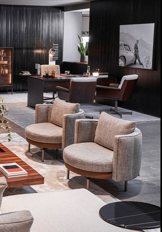 A modern office with two grey armchairs, a wooden table, dark panelled walls, lush plants, and sleek contemporary decor.