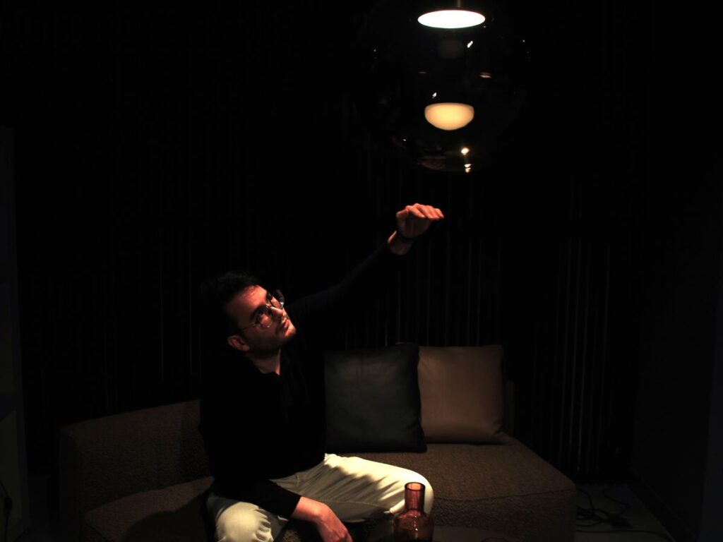 James Apichart Jarvis reaches up, bathed in the glow of a Brokis Orbis pendant overhead.