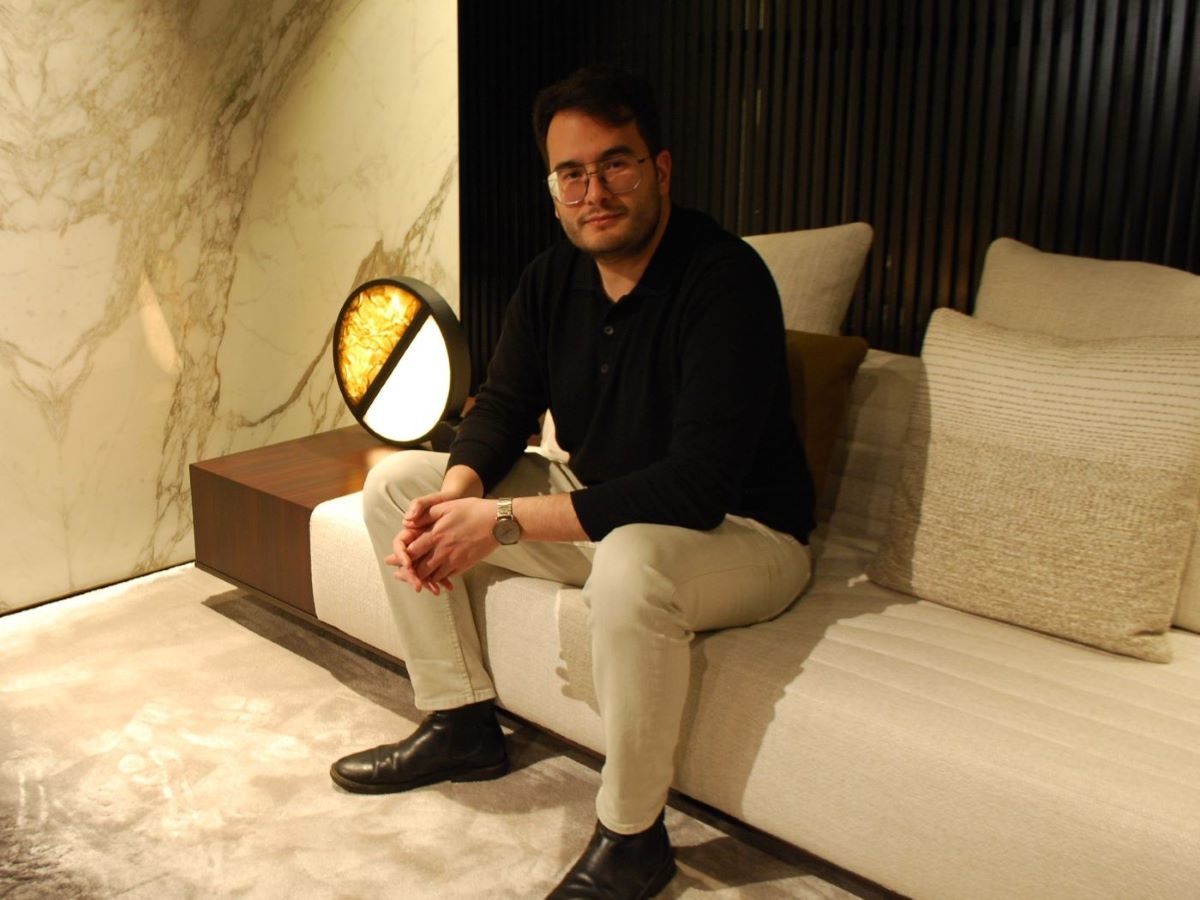 James Apichart Jarvis sits on a modern light sofa, framed by Brokis Geometric Table, marble wall, and plush beige cushions.