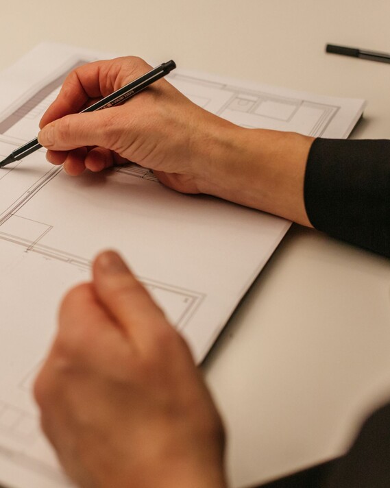 A person in a dark sleeve sketches on an architectural floor plan at a light table, softly illuminated by elegant lighting.