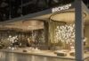 Euroluce 2025 stand showcases Brokis glass lighting, sculptural pendants, warm tones, and elegant curved drapes.