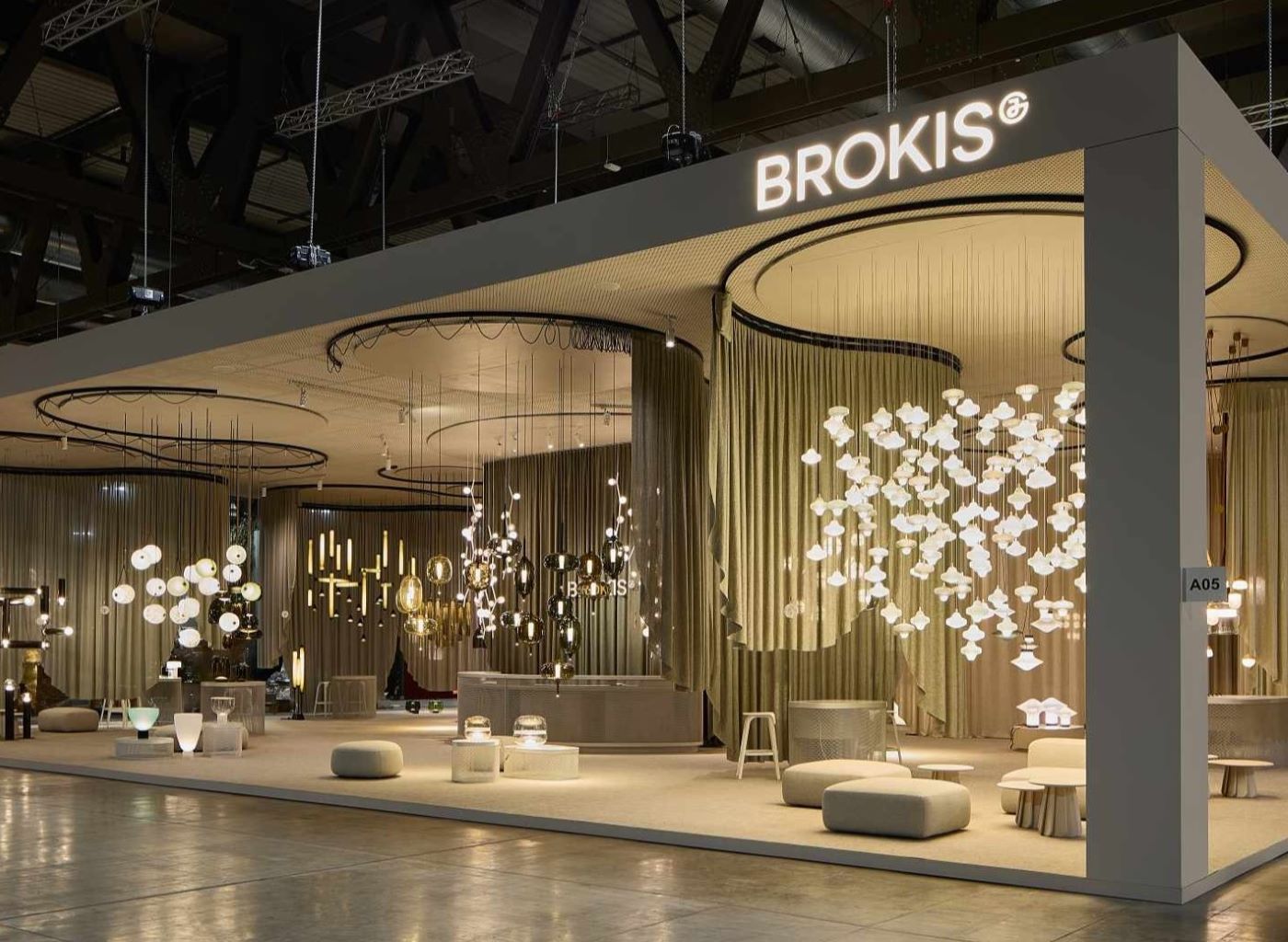 Euroluce 2025 stand showcases Brokis glass lighting, sculptural pendants, warm tones, and elegant curved drapes.