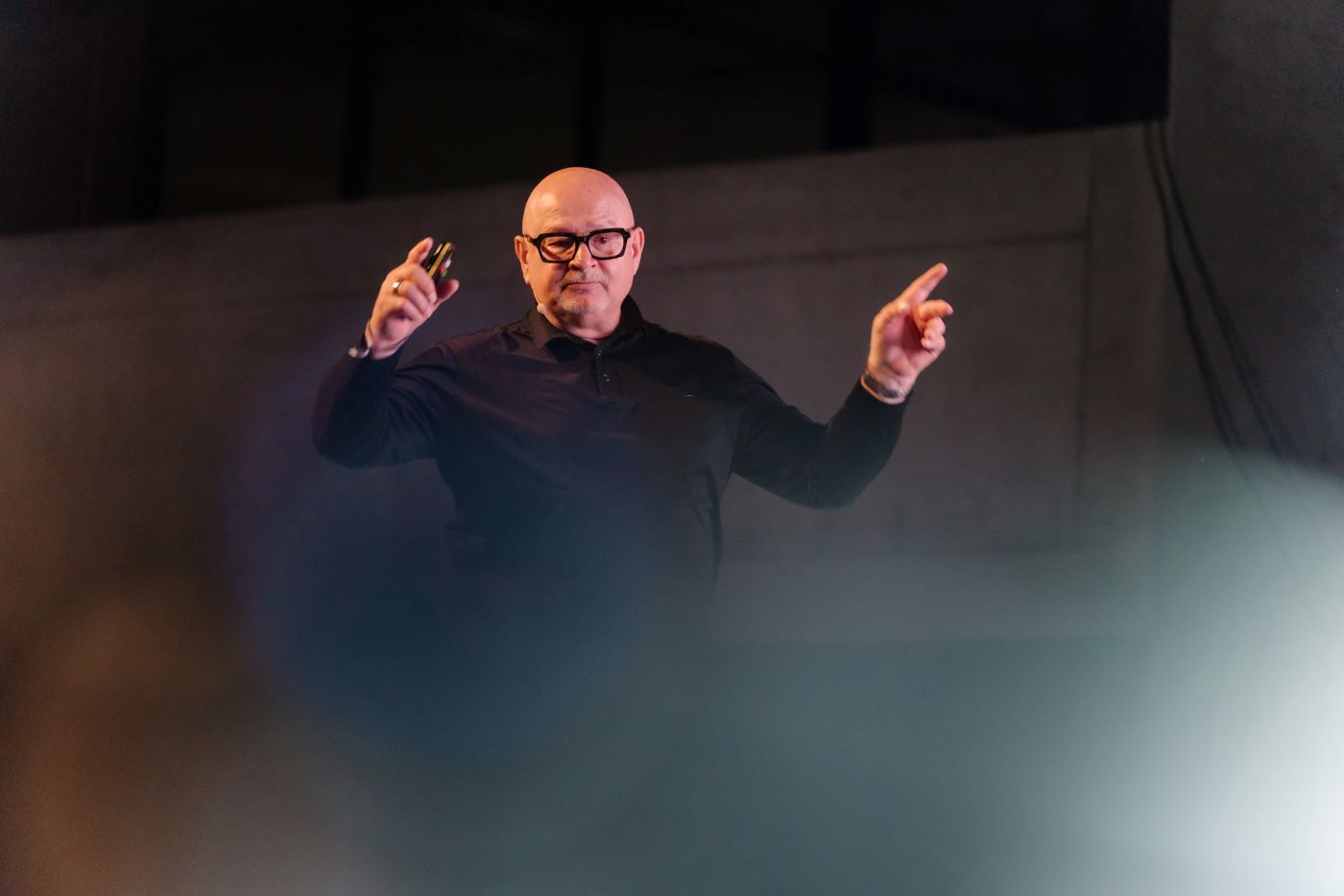 Jan Rabell commands the stage, remote in hand, softly lit against a moody, elegantly dim backdrop.