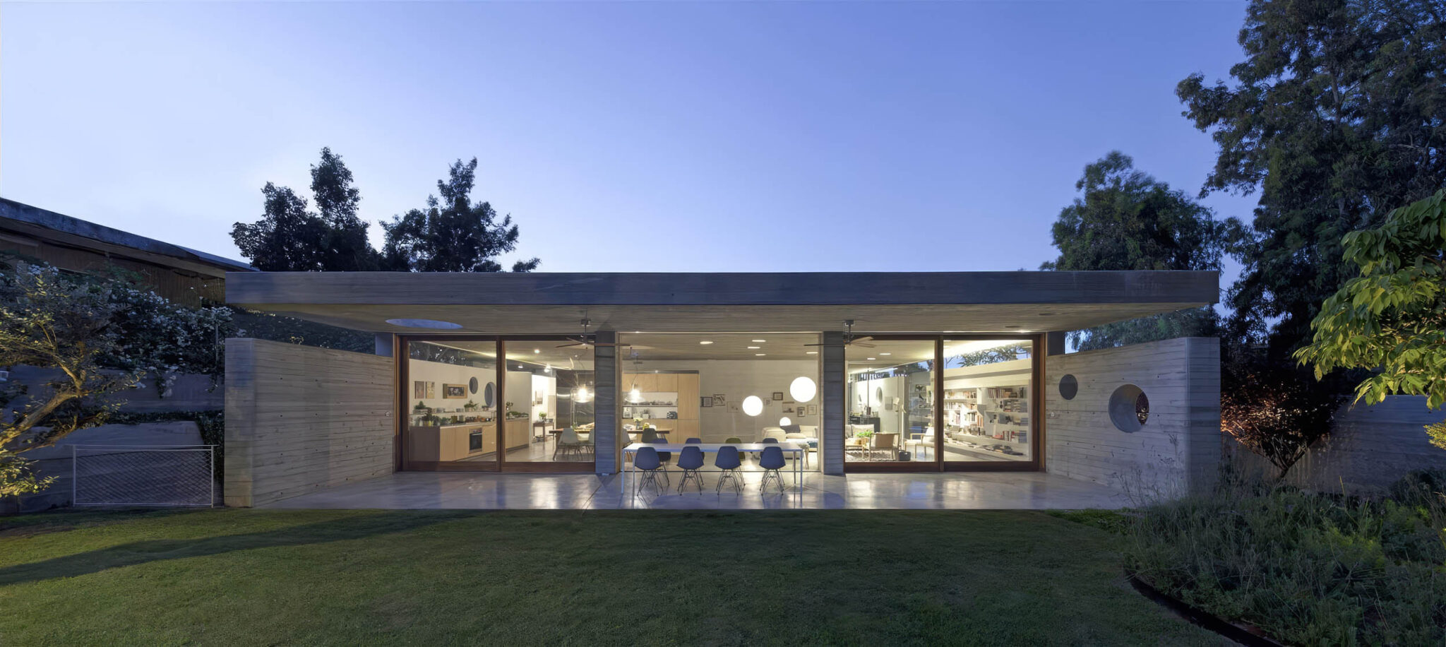 Modern single-storey home with expansive glass walls, sleek concrete roof, and Brokis lighting glowing at dusk.