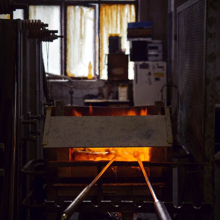 Two metal rods glow in an orange-hot furnace amid dim, atmospheric lighting and industrial Brokis details in the background.