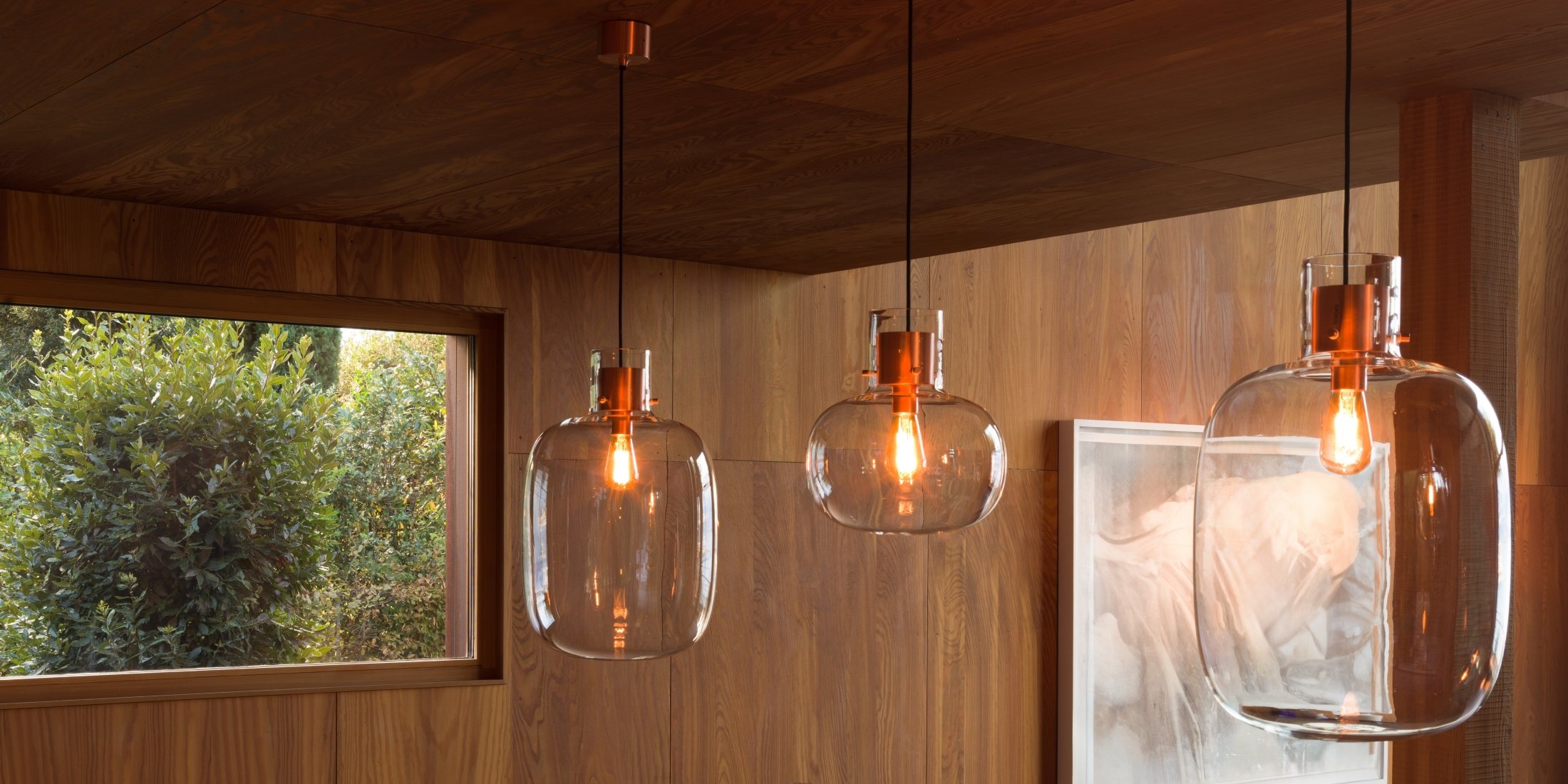 Brokis Awa pendants glow above wood panelling; lush greenery and elegant art complete the refined space.