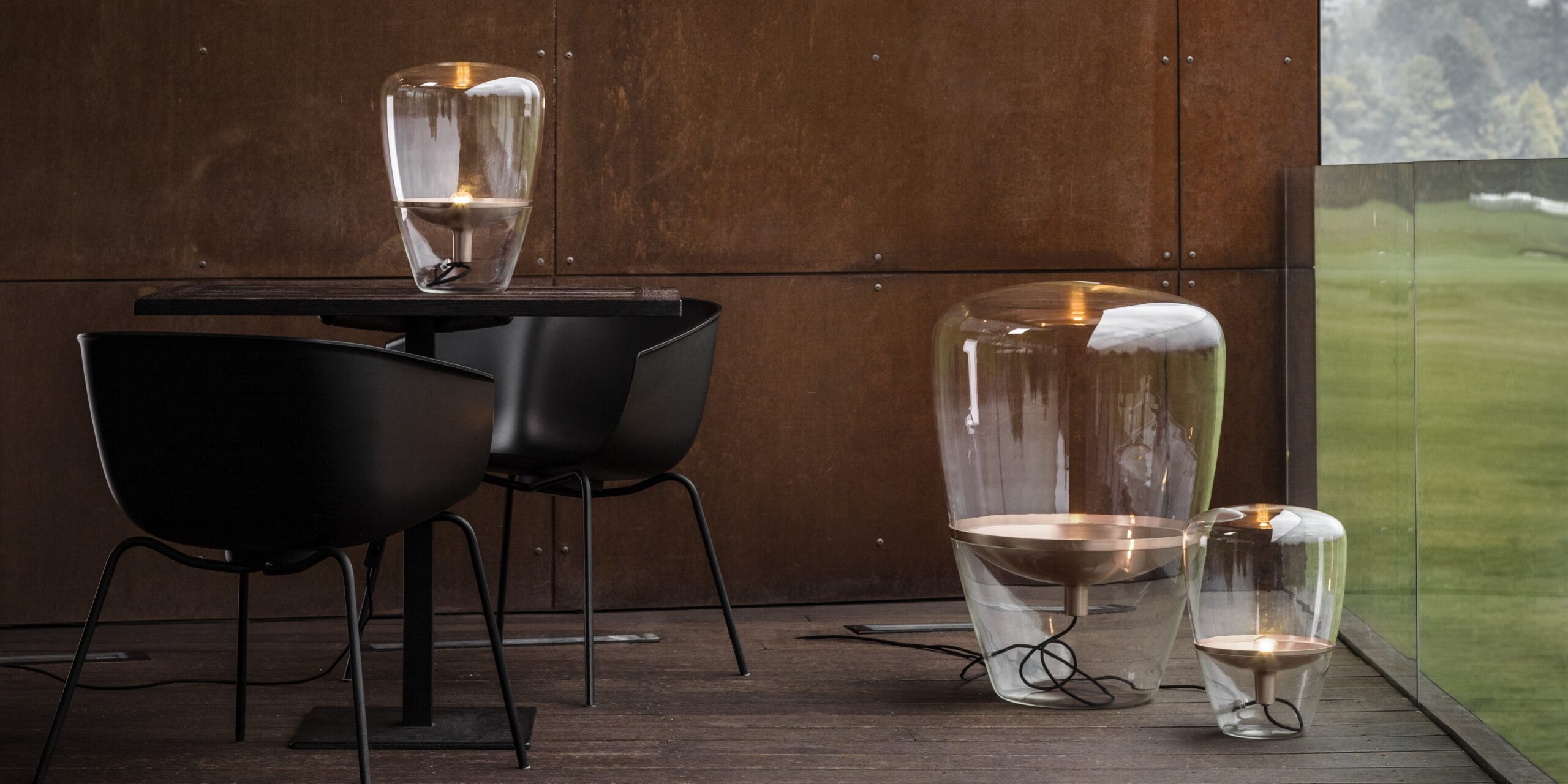 Brokis Balloons lamps glowing on the floor, on a modern terrace with black chairs, and a dark wood table.