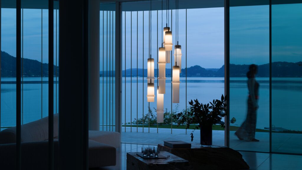 Brokis Bamboo Forest pendants in a modern living room at dusk with vast glass windows framing a tranquil lake.