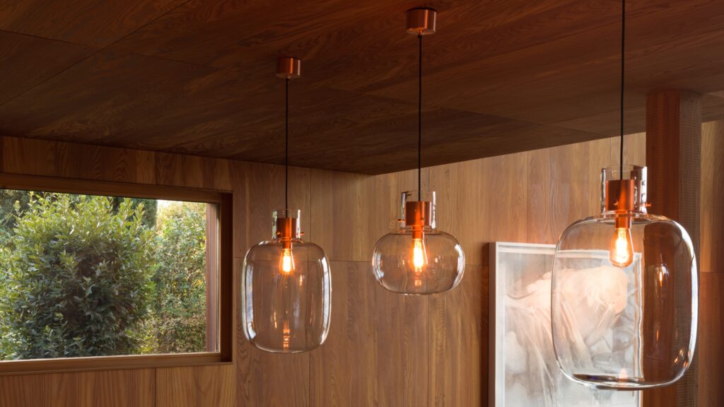 Brokis Awa pendants with clear shades glow in a wood-panelled room washed with natural light.
