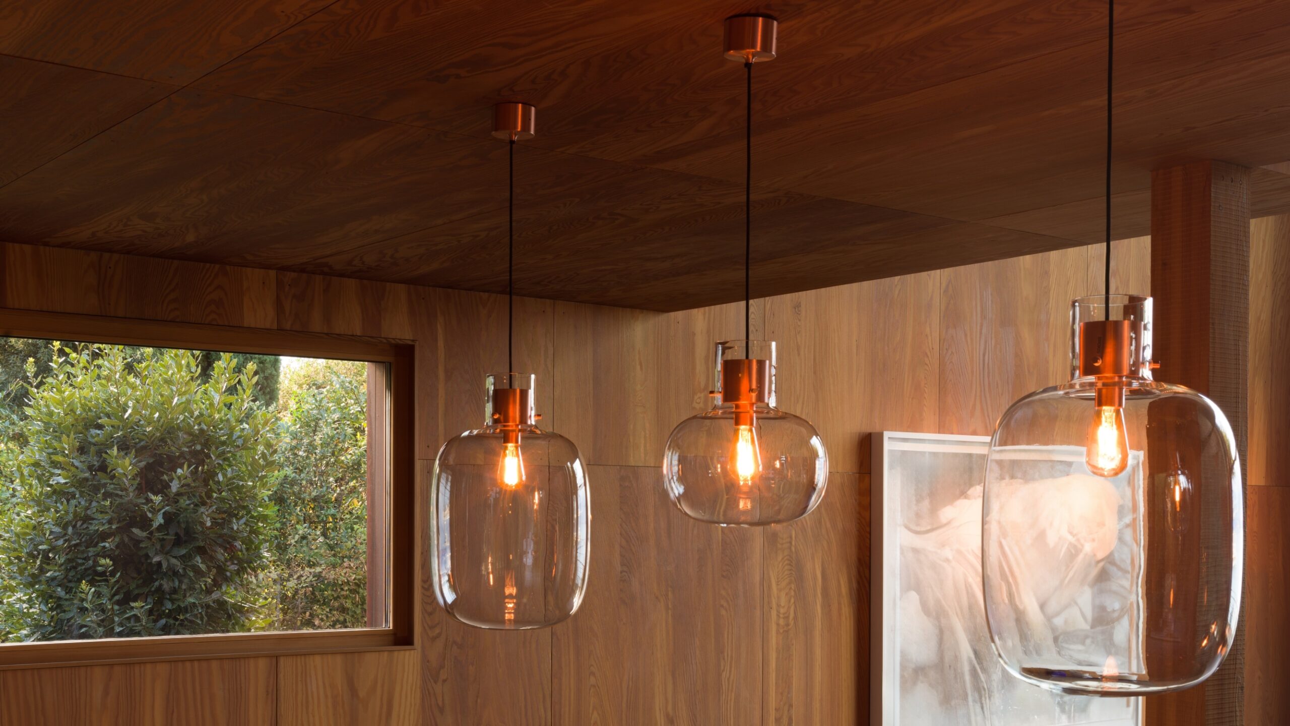 Brokis Awa pendants with clear shades glow in a wood-panelled room washed with natural light.