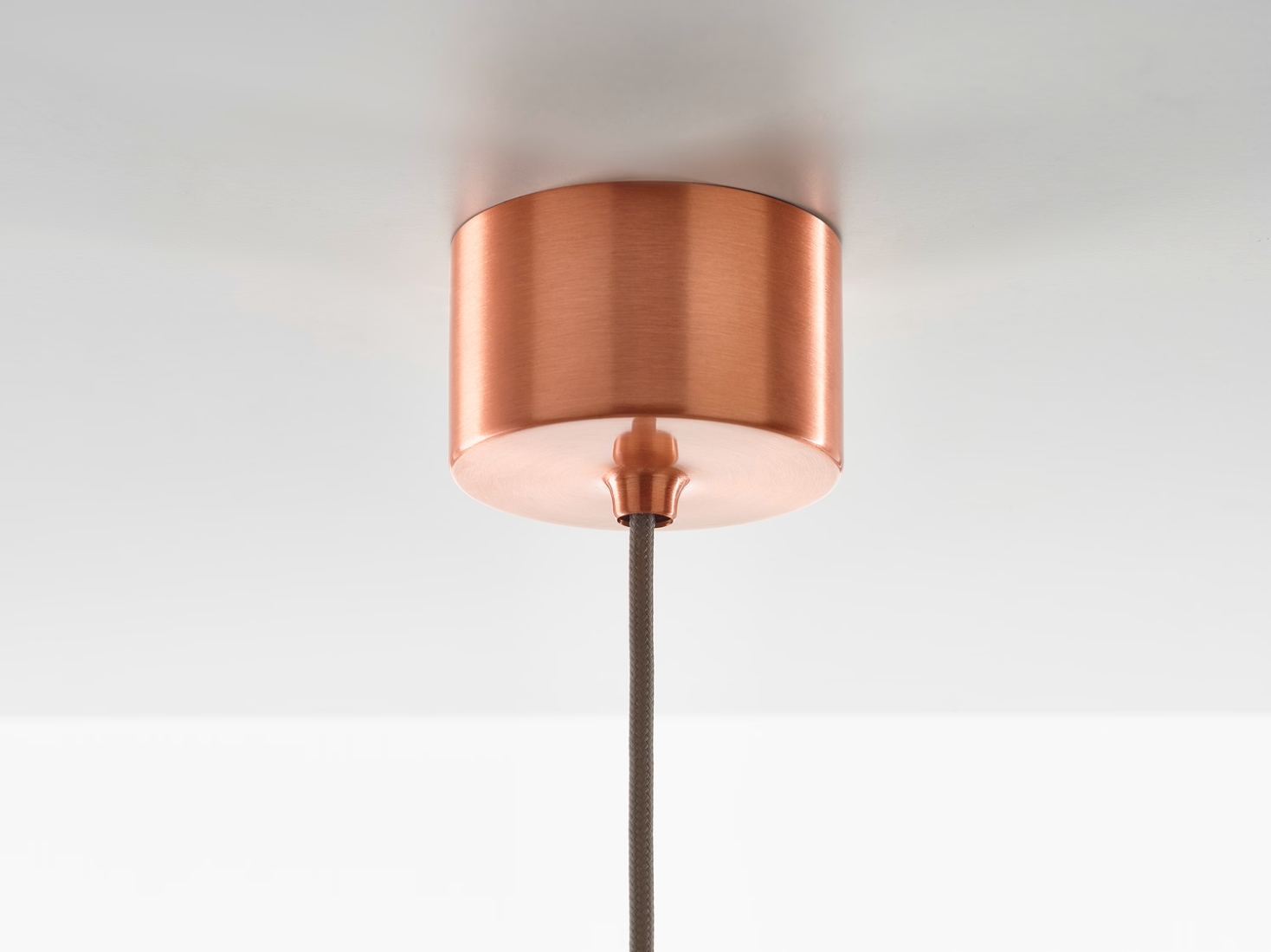 A close-up of a Brokis Awa copper ceiling canopy with cylindrical form and grey fabric flex, flush against a white ceiling.