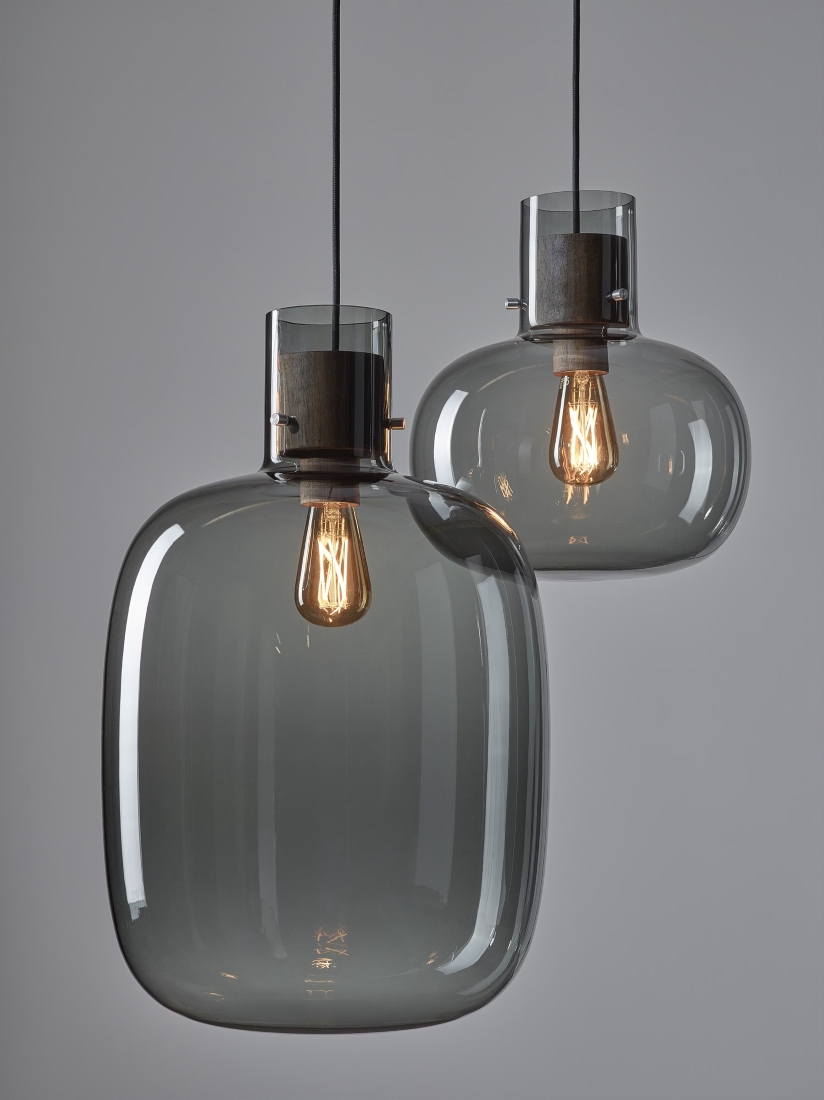 Handblown Brokis Awa pendant lights in smoky crystal glass, Edison bulbs aglow, exude minimalist luxury against a pale backdrop.
