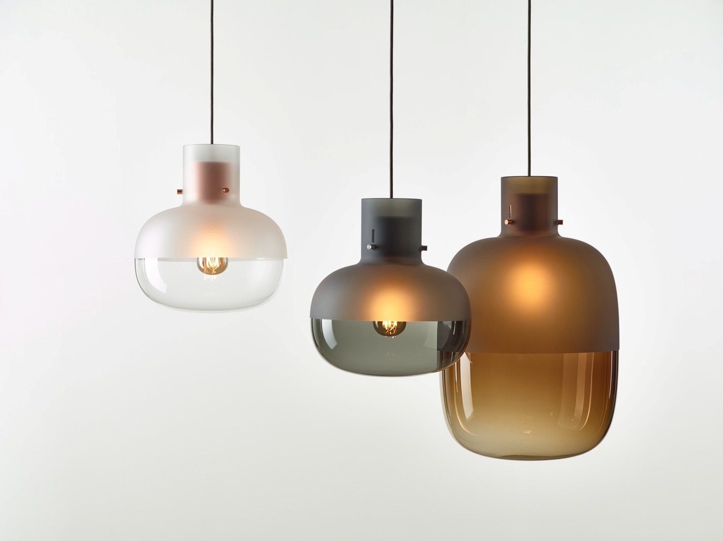 Brokis Awa pendants - white opaque, smoke grey, and brown glass - hang side by side with exposed bulbs in each.
