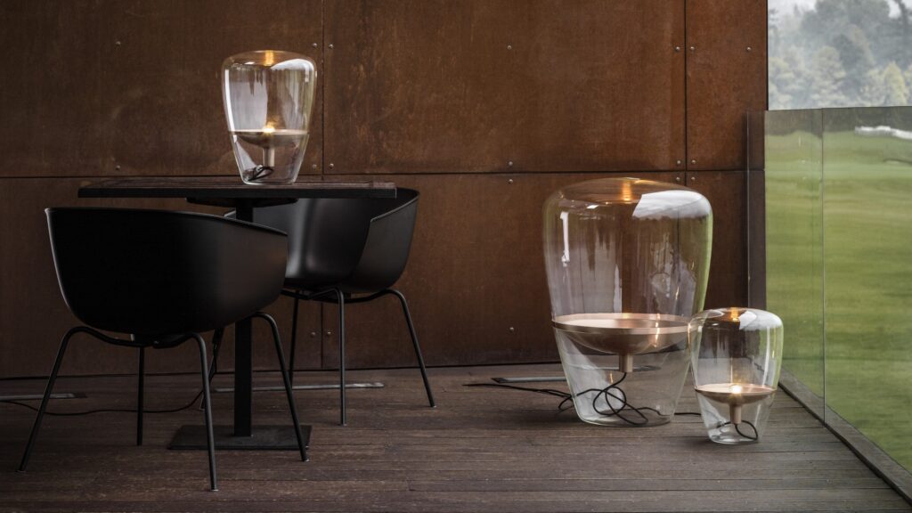 Brokis Balloons lamps glow warmly on a modern patio with black chairs, dark wood table, above lush outdoor views.