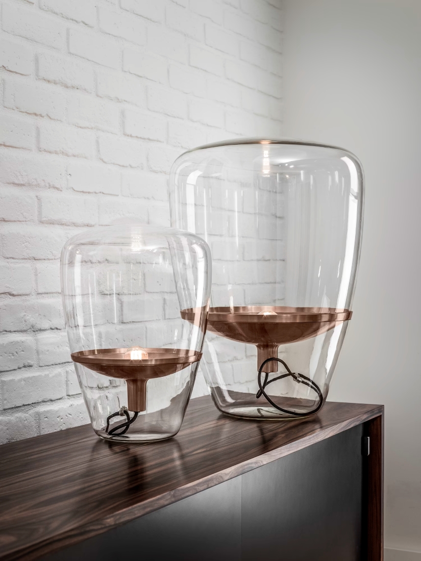 Brokis Balloons glass table lamps with copper bases grace a dark wood cupboard against a white brick wall.