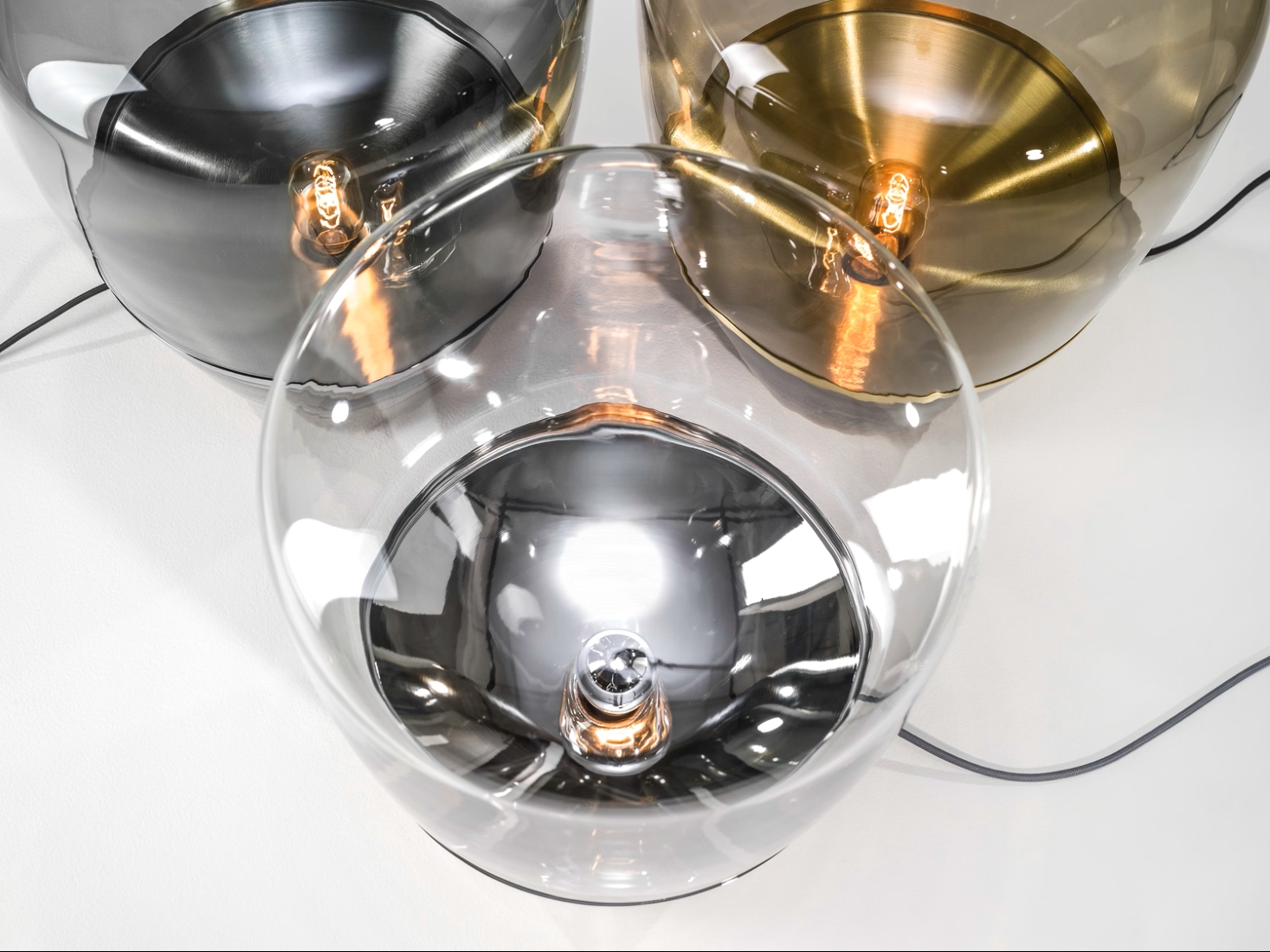 Brokis Balloons glass lamps with glowing bulbs in clear, grey, and brass, artfully arranged on white.