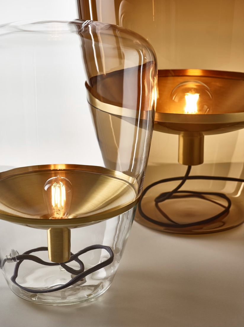 Brokis Balloons lamps with handblown glass domes and brass bases emit a warm, luxurious glow on a white surface.