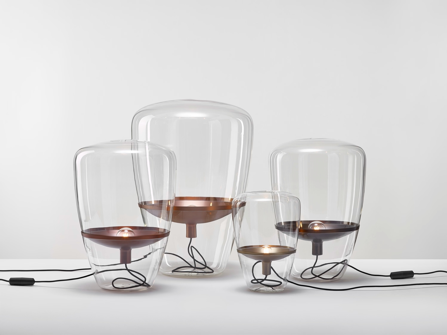 Brokis Balloons lamps with clear glass domes and lustrous metal bases glow elegantly on a pristine white surface.