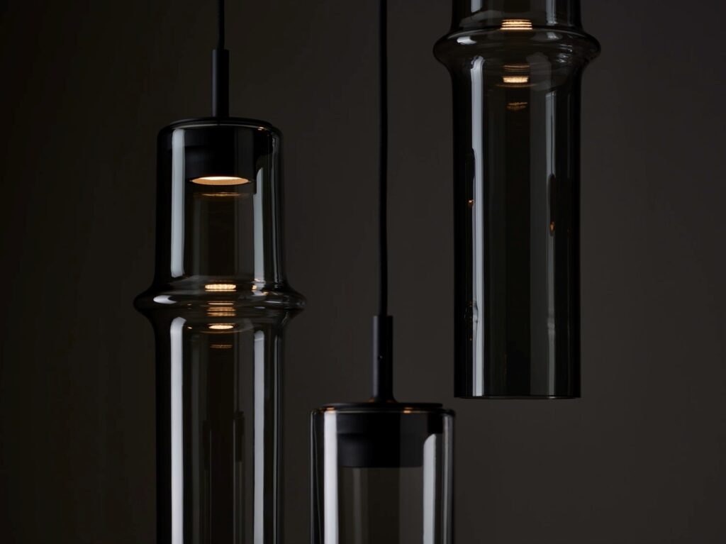 Brokis Bamboo Forest pendants in handblown brown glass emit a warm glow, casting luxe reflections against a dark backdrop.