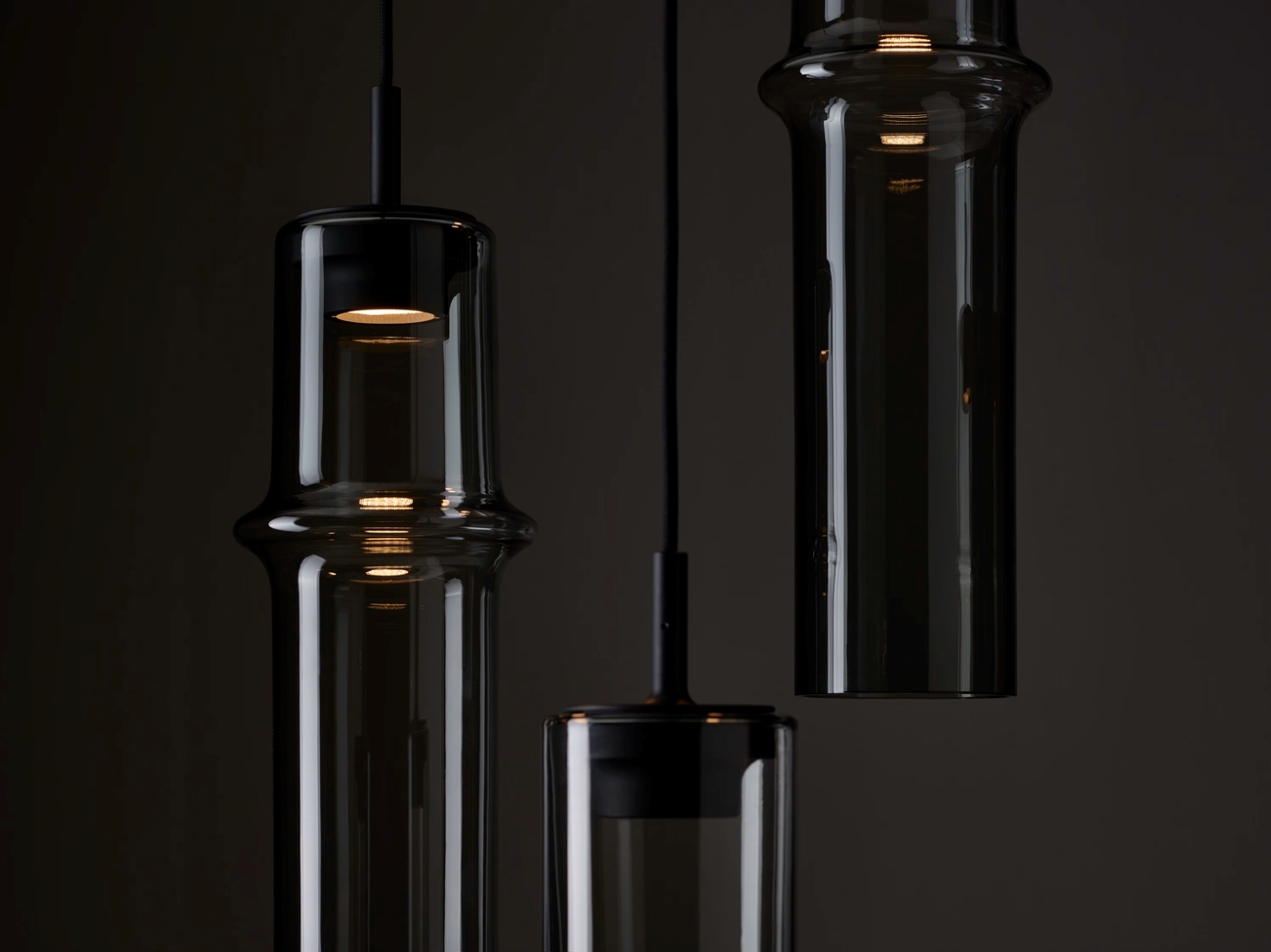 Brokis Bamboo Forest pendants in handblown brown glass emit a warm glow, casting luxe reflections against a dark backdrop.