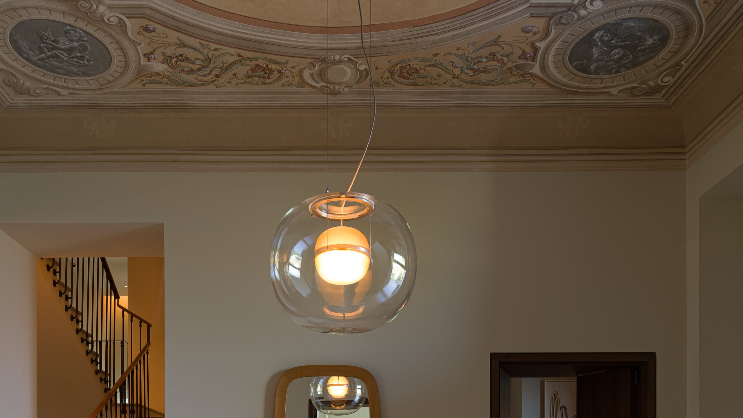 Brokis Big One Large pendant glows beneath an ornate frescoed ceiling; a staircase and mirror accentuate the elegant scene.
