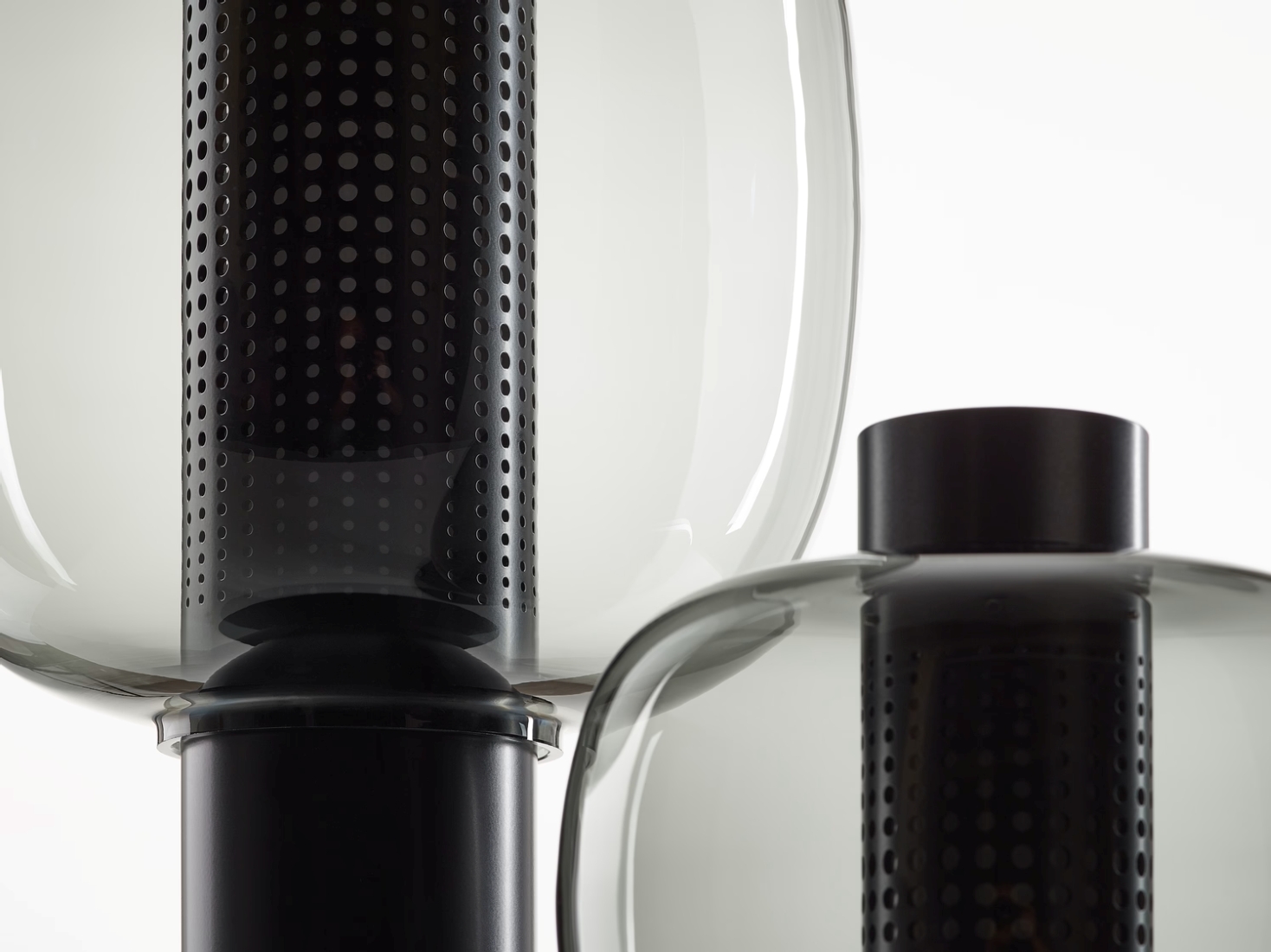 Close-up of two Brokis Bonbori lamps with smoke grey glass and perforated black metal cylinders.