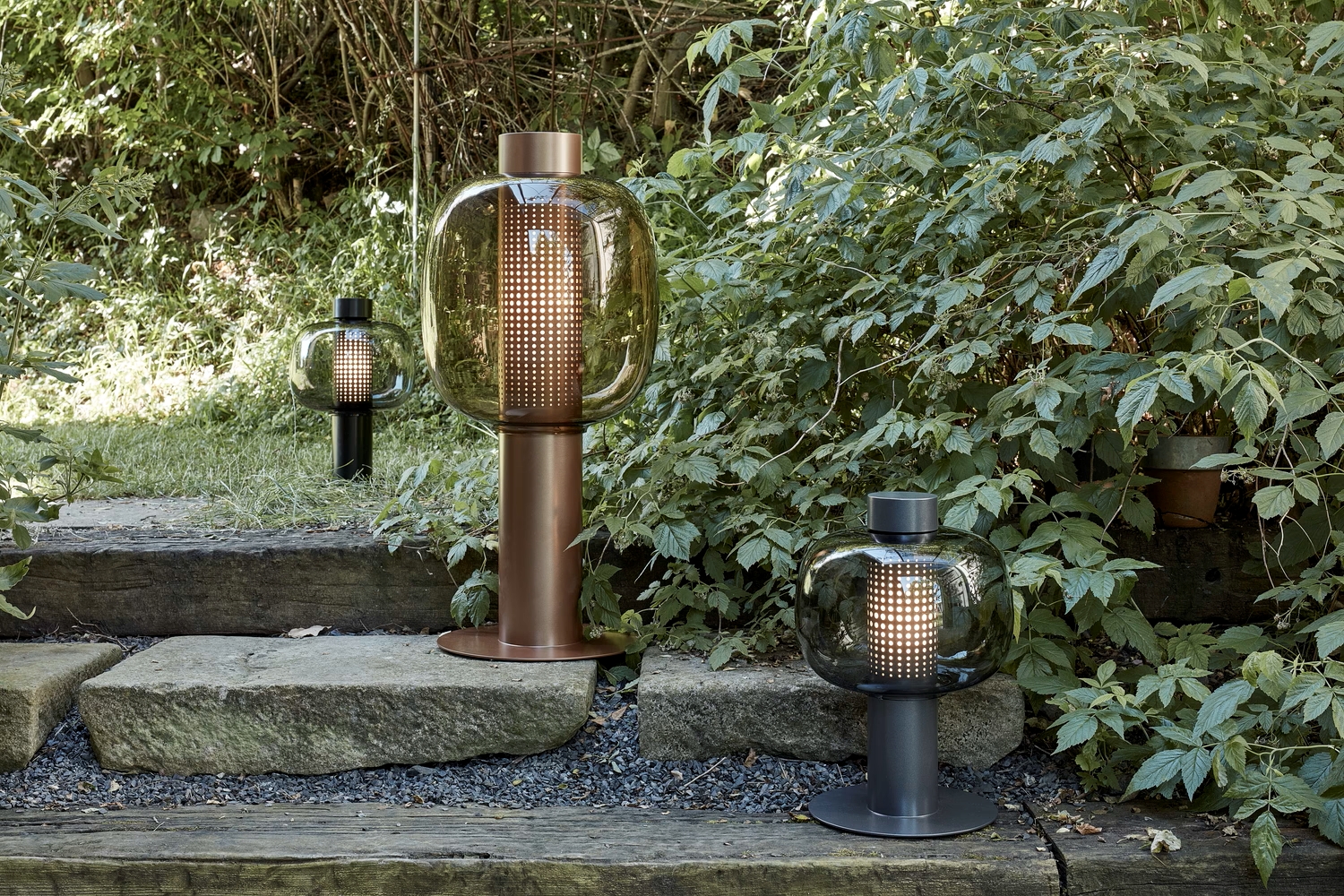Brokis Bonbori Outdoor lamps with domed glass illuminate stone steps amid lush garden greenery.
