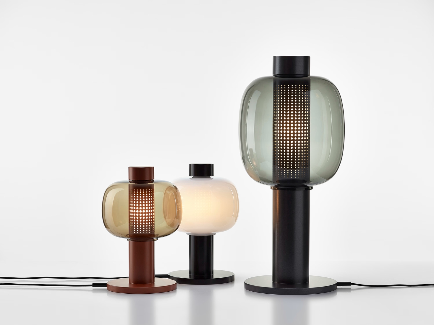 Trio of Brokis Bonbori lamps with rounded glass shades in brown, opaline, and grey on a pristine white surface.