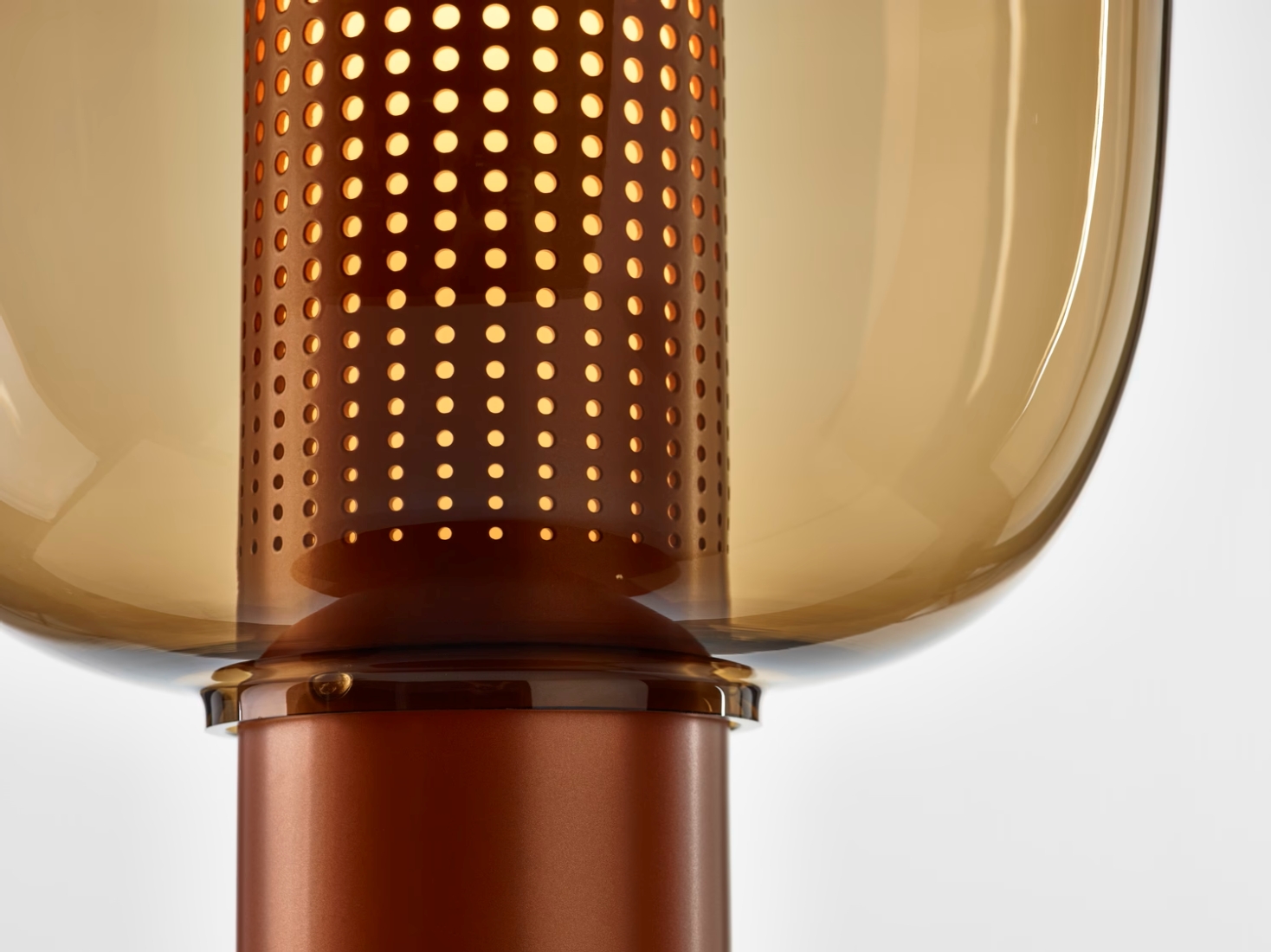 Close-up of a Brokis Bonbori lamp; warm light glows through perforated copper base and brown glass.
