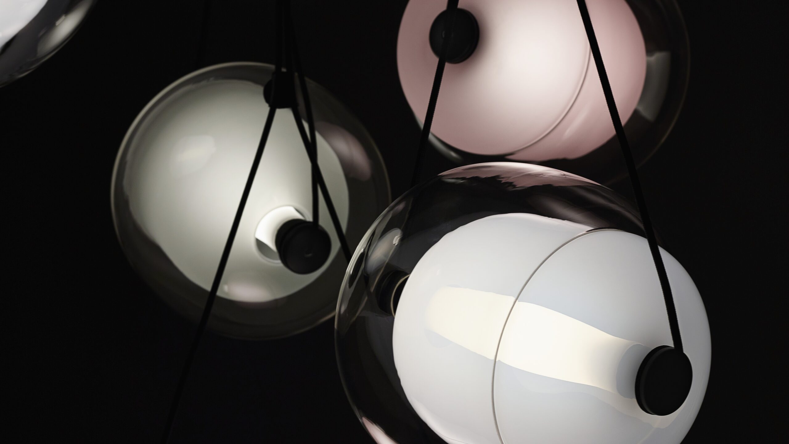 Brokis Capsula pendants with handblown glass spheres in white to violet, glowing against a dark backdrop.