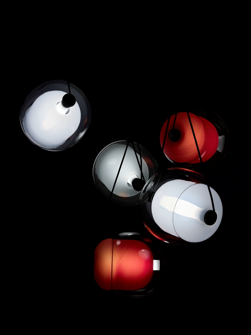 Brokis Capsula Set Metal Canopy in handblown glass emit soft white and red glows against a dramatic black backdrop.
