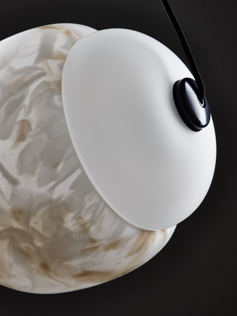 A close-up of a Brokis Capsula light with handblown BROKISGLASS in beige and white, floating against a dark background.