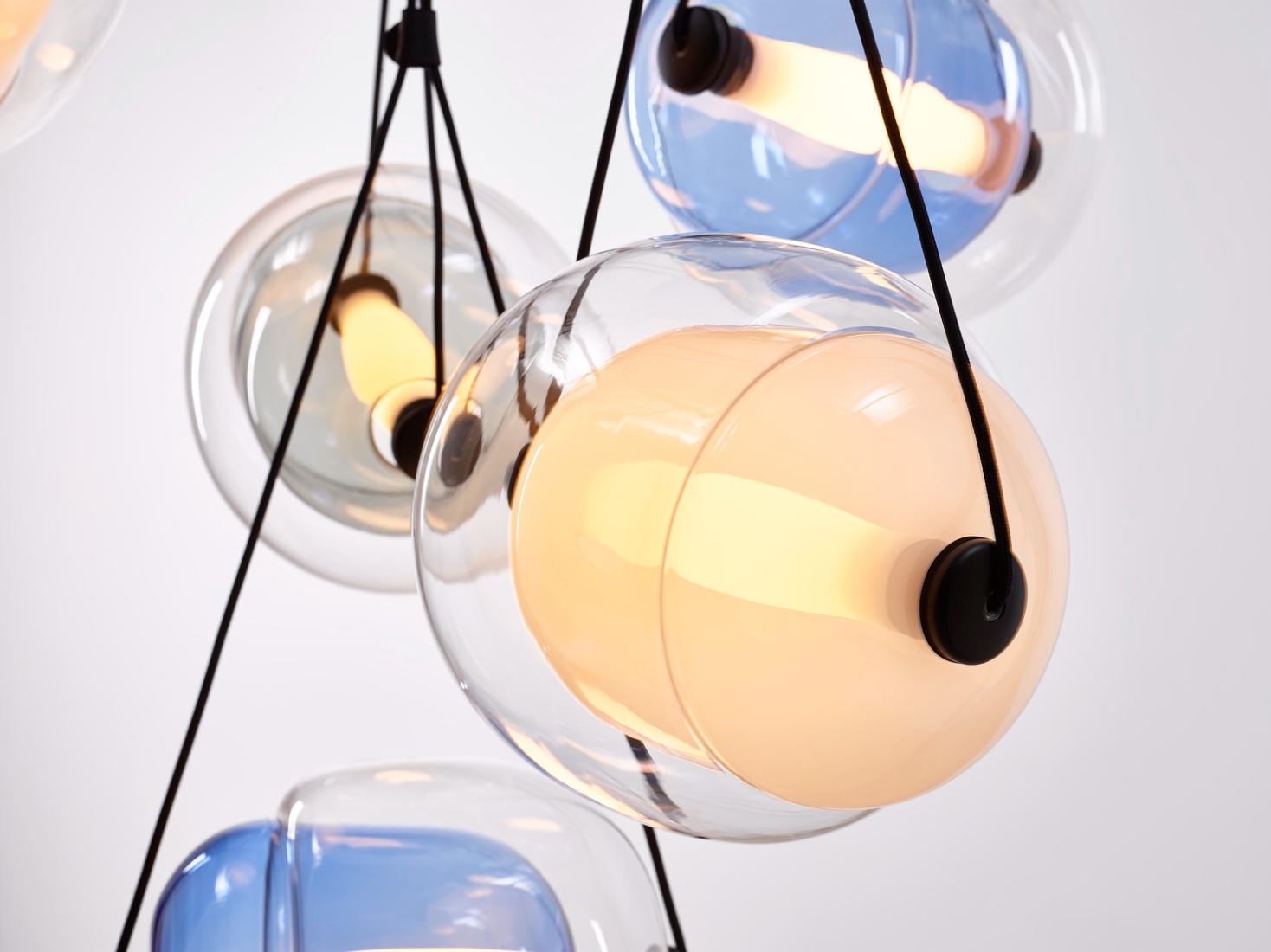 Close-up of Brokis Capsula Single pendants in clear, blue, and amber crystal, each globe encasing a tubular LED.