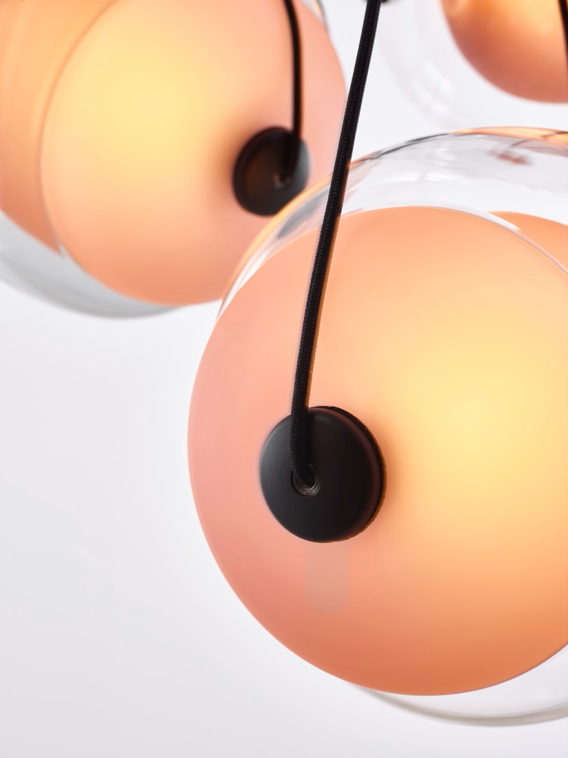Close-up of two Brokis Capsula Single pendants in frosted amber glass, softly glowing against a white gradient.