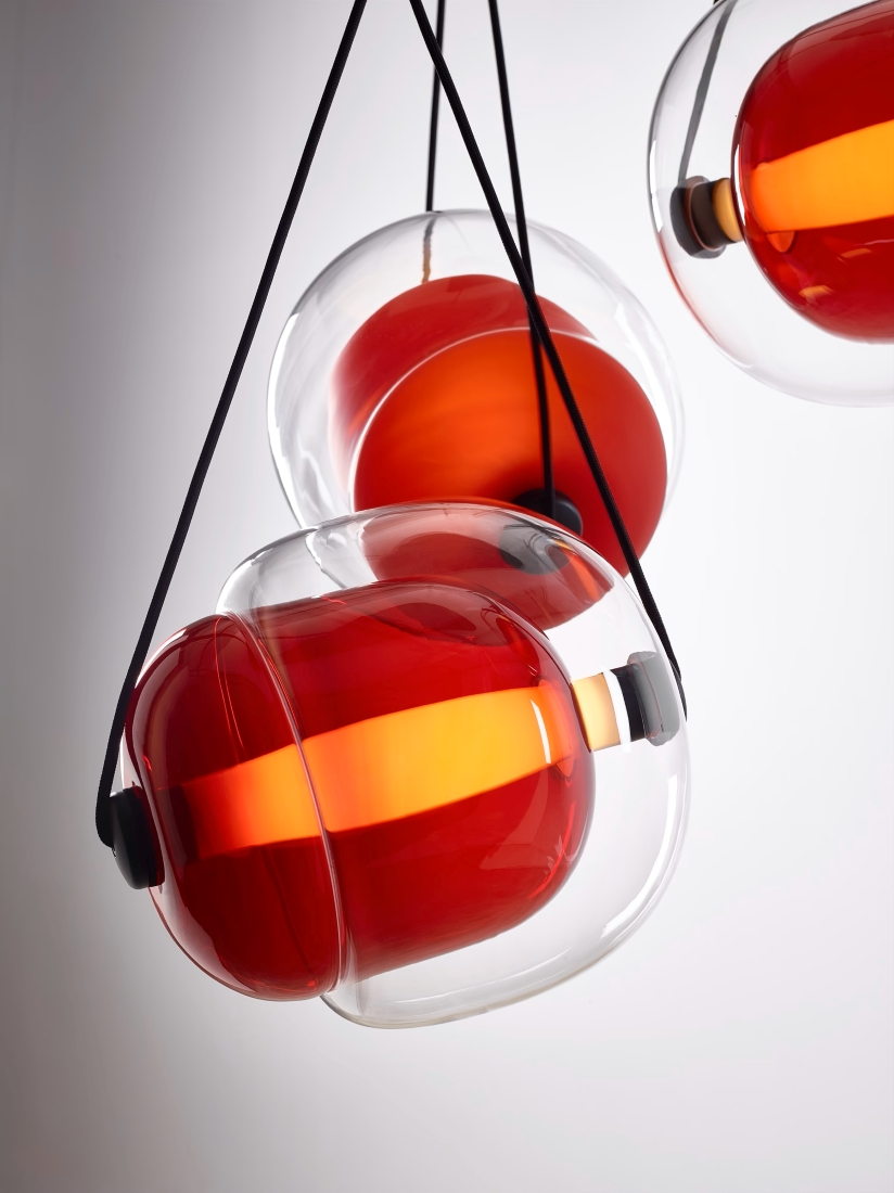 Brokis Capsula pendants in clear glass with glossy red interior glow warmly, suspended by sleek black cords.